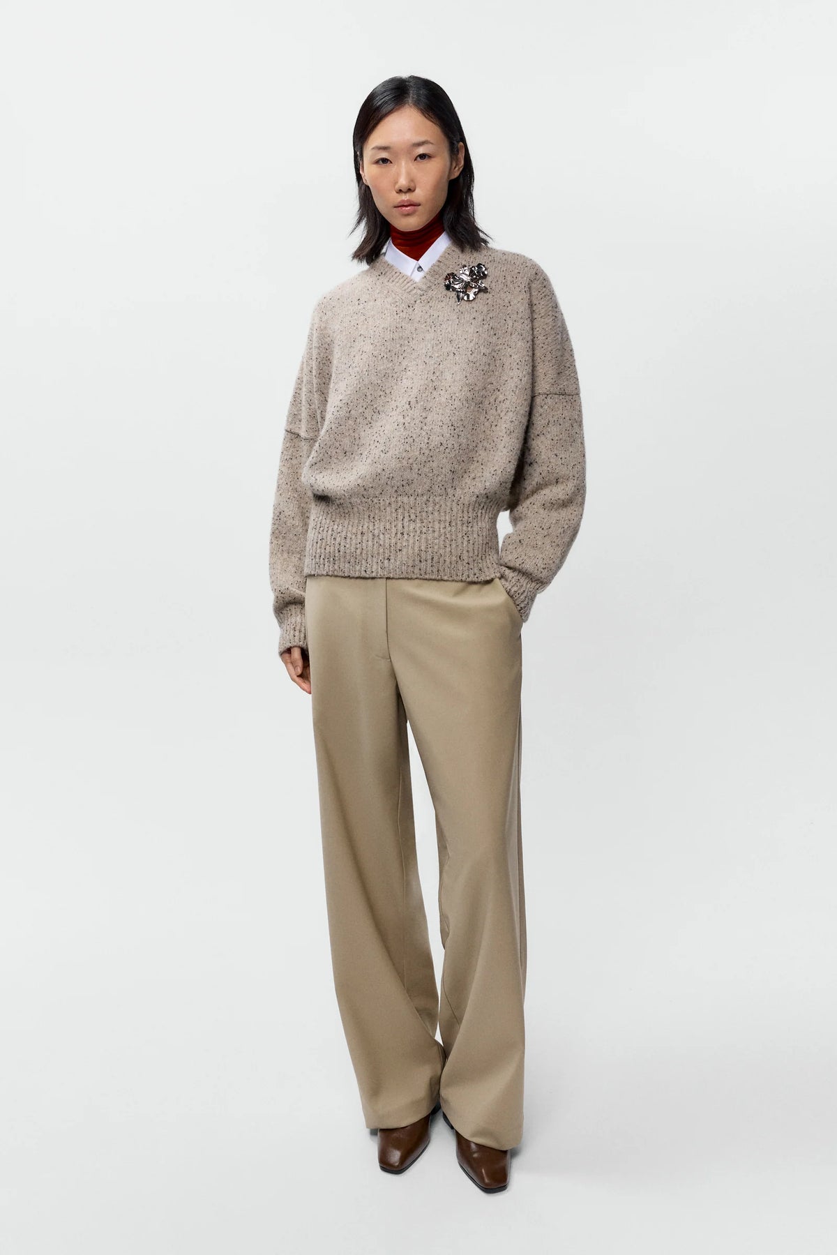Person wearing a beige sweater and beige pants on a white background
