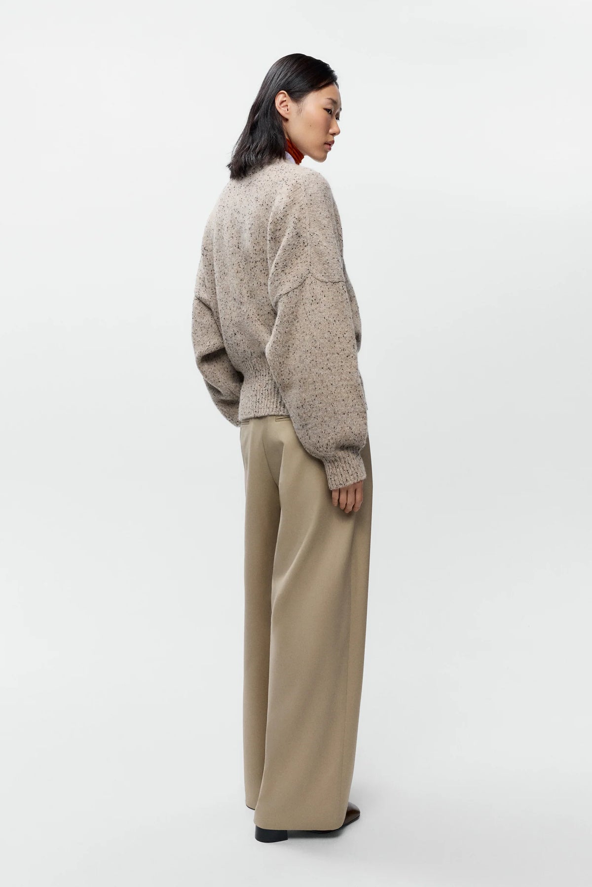 A model shown from the back wearing a fuzzy, textured beige knit sweater and wide-leg beige trousers against a plain light gray studio background.
