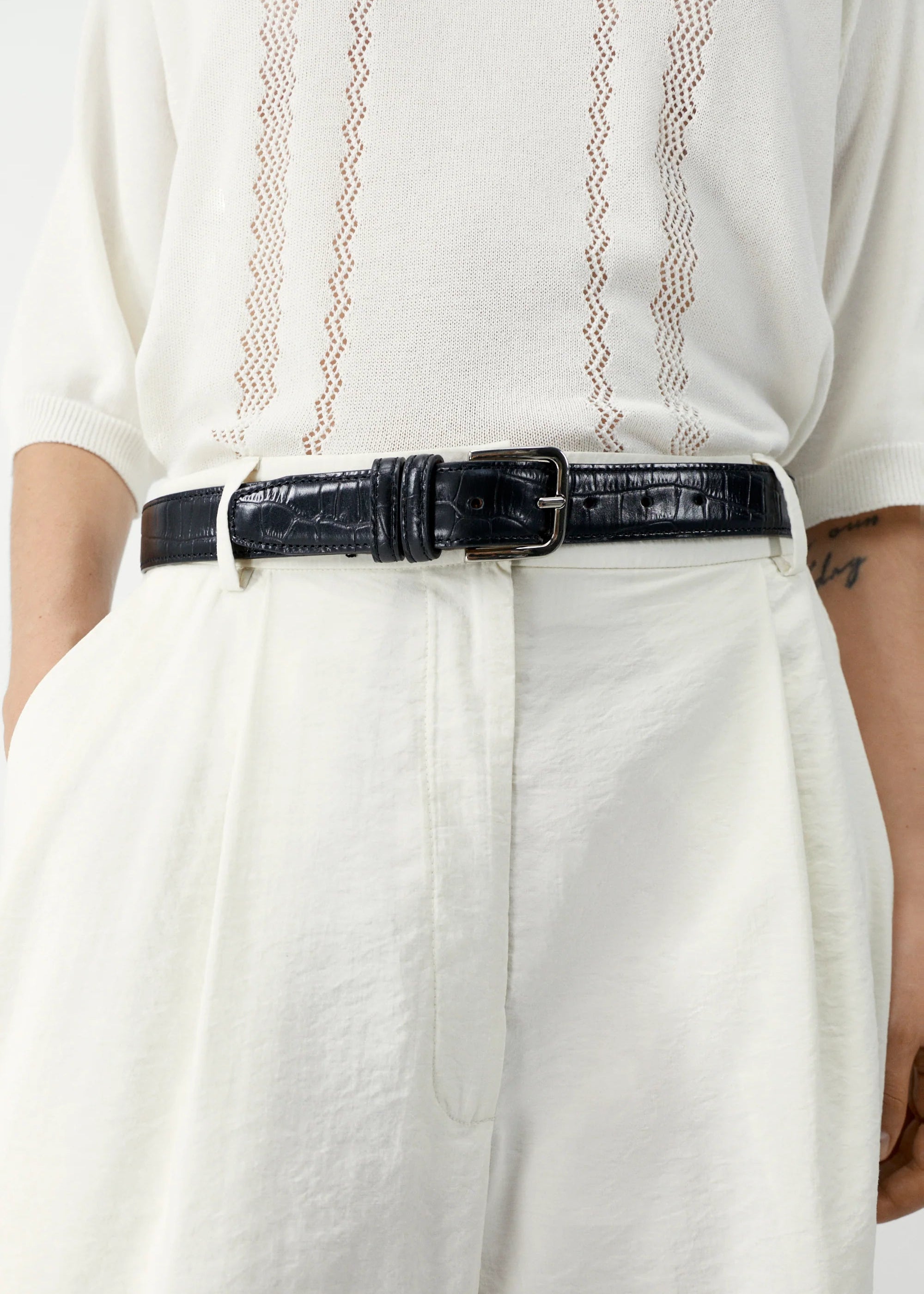 Person wearing a white outfit with a black belt on a plain background