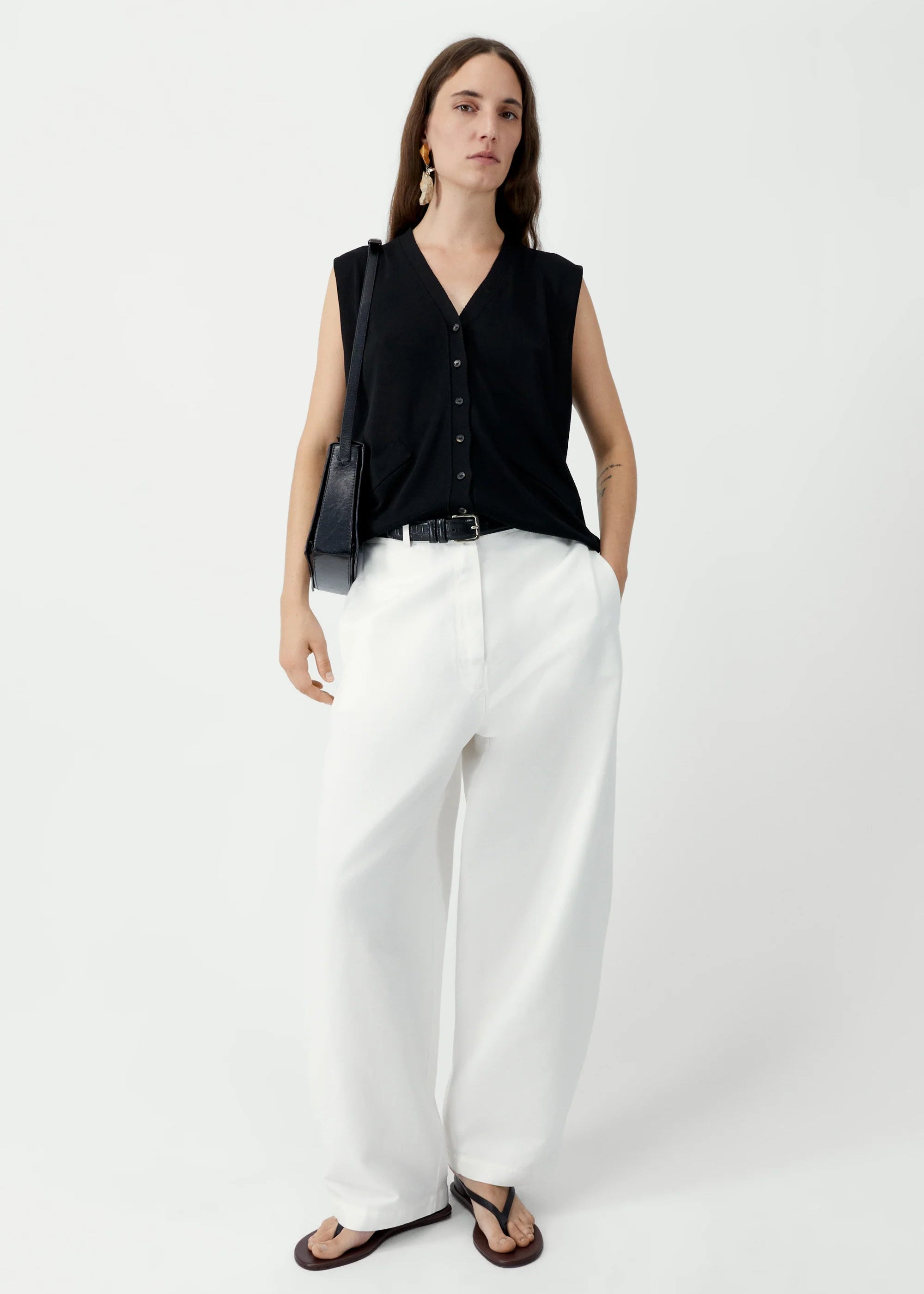 Woman wearing a black sleeveless top and white pants on a white background