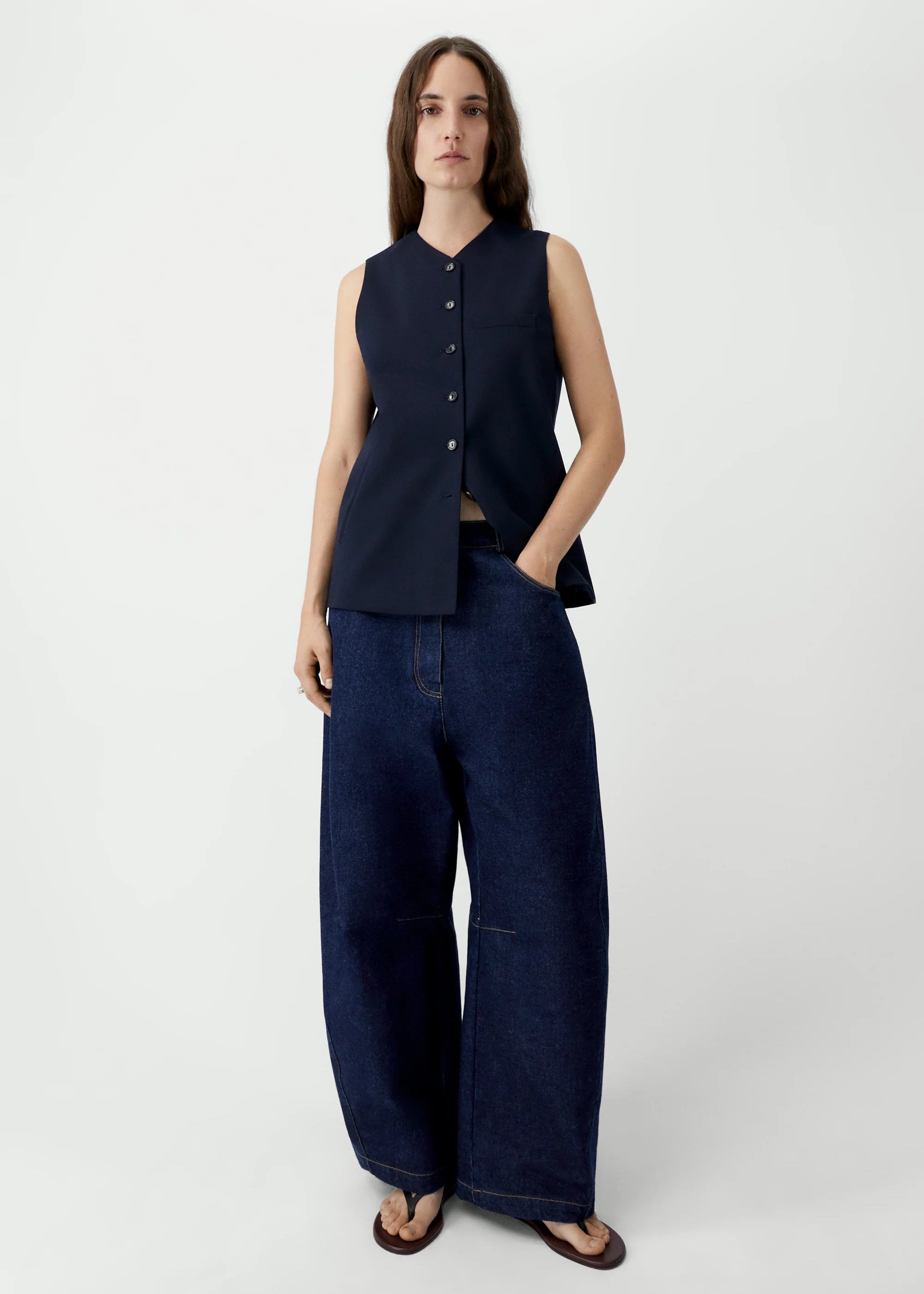 Woman wearing a dark blue sleeveless top and wide-leg jeans on a white background