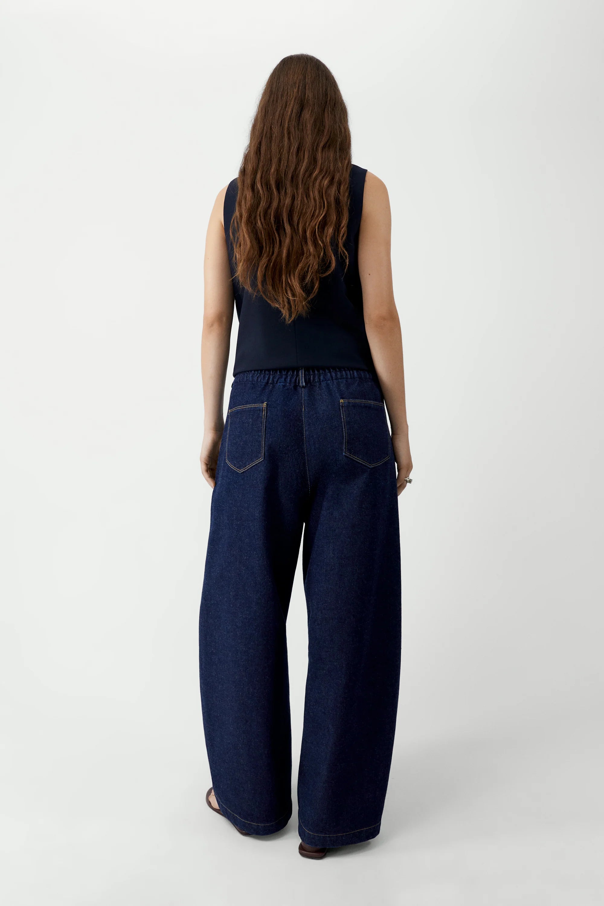 Person wearing dark blue jeans and a black sleeveless top on a white background
