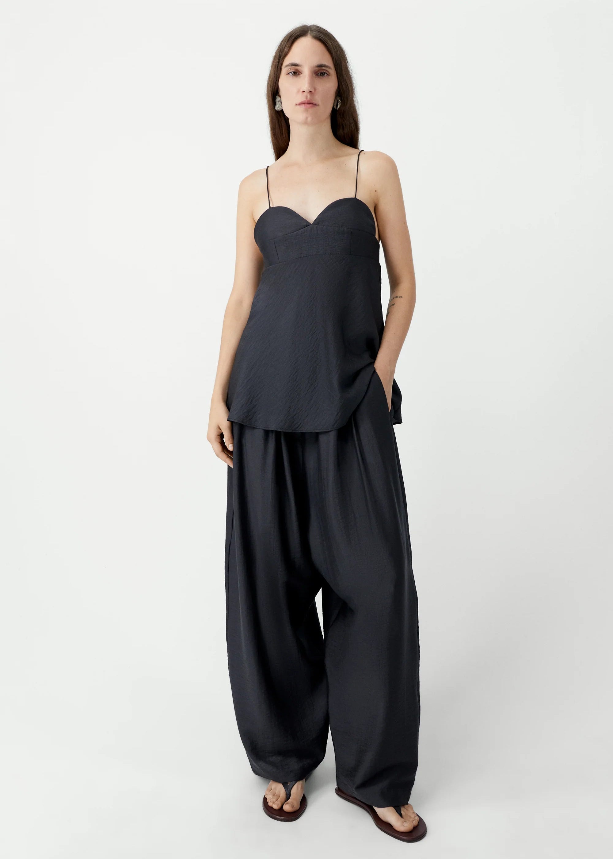 Woman wearing a black sleeveless top and wide-leg pants on a white background