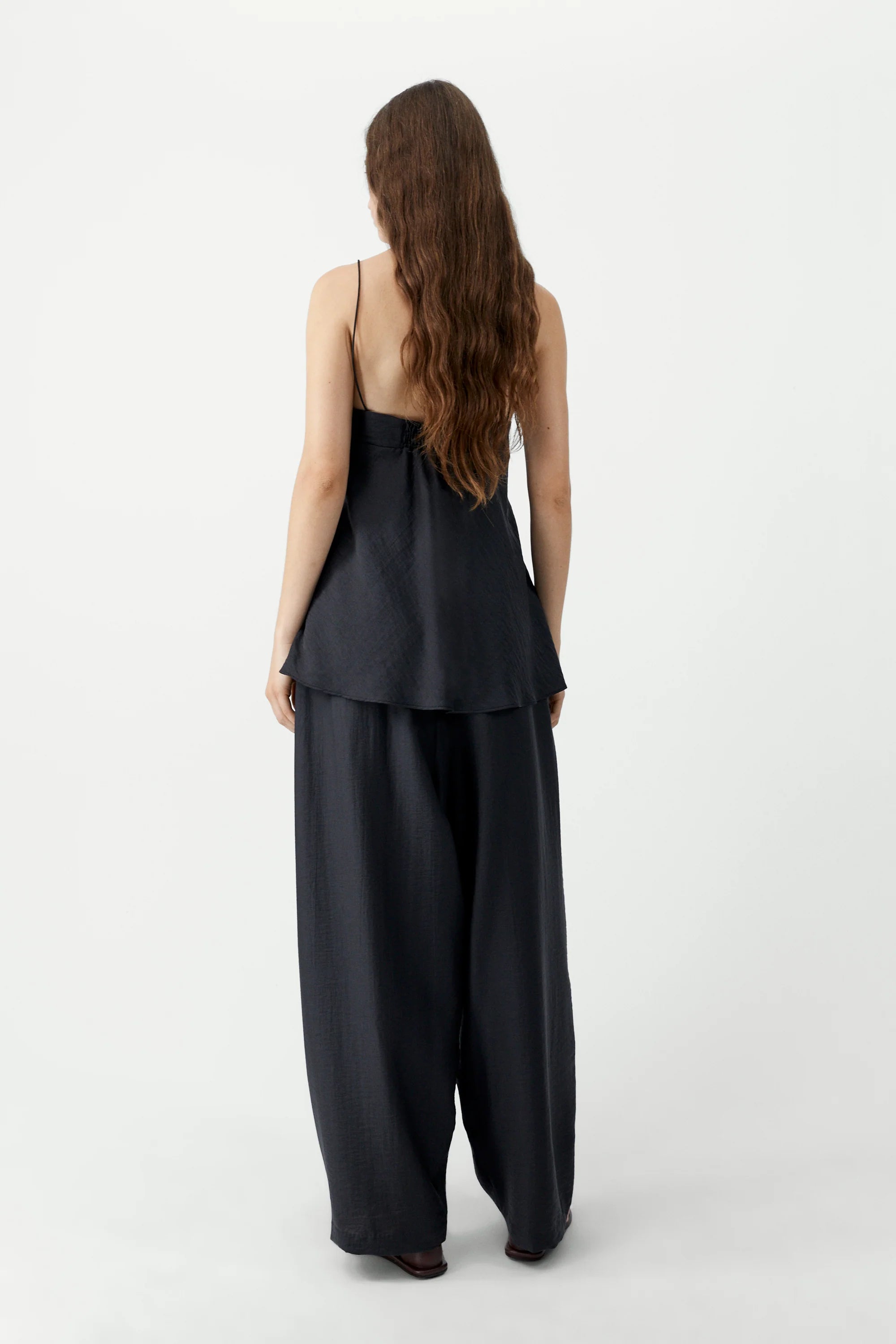 Woman wearing a black outfit with wide-leg pants on a white background