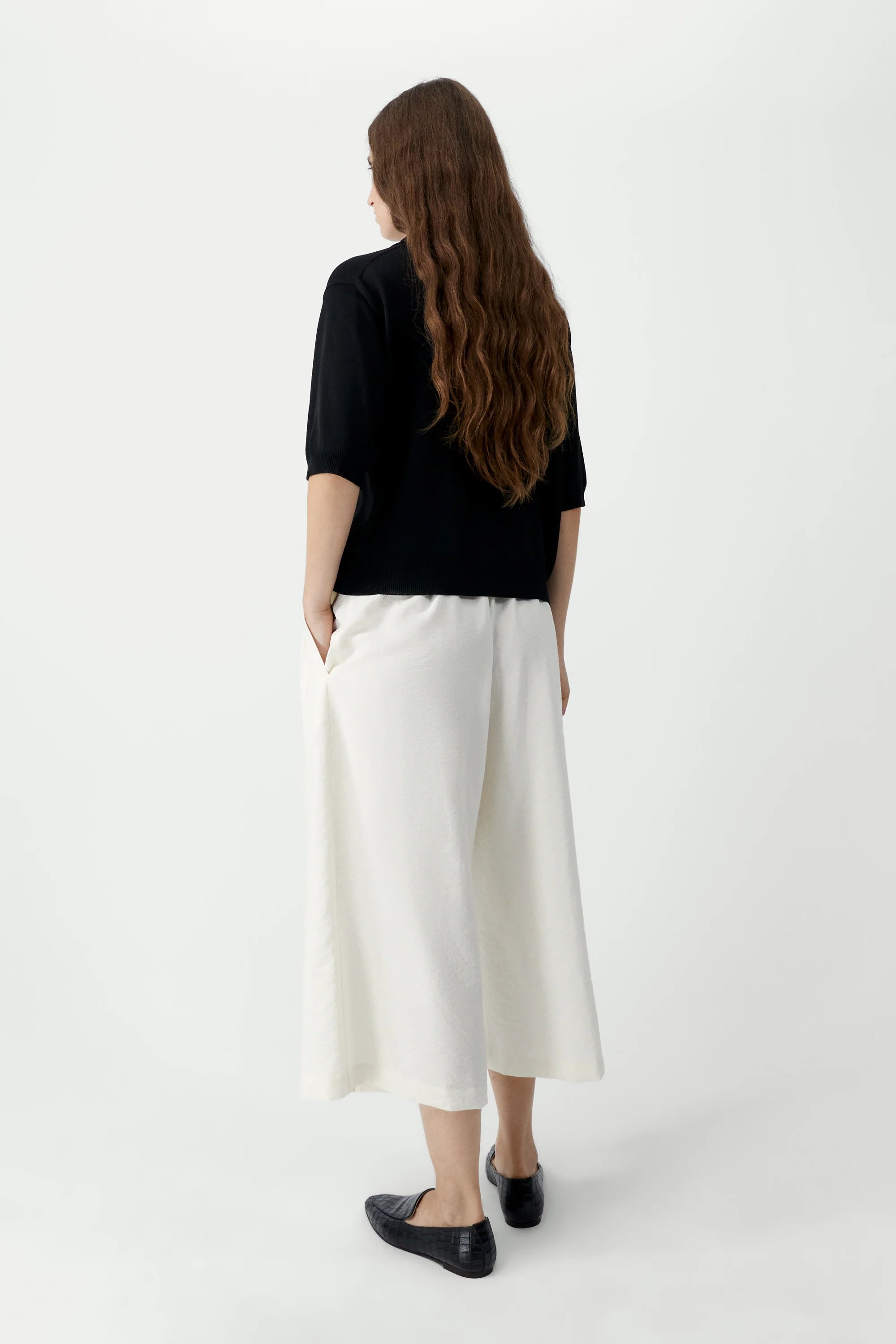 Person wearing a black top and white pants on a white background
