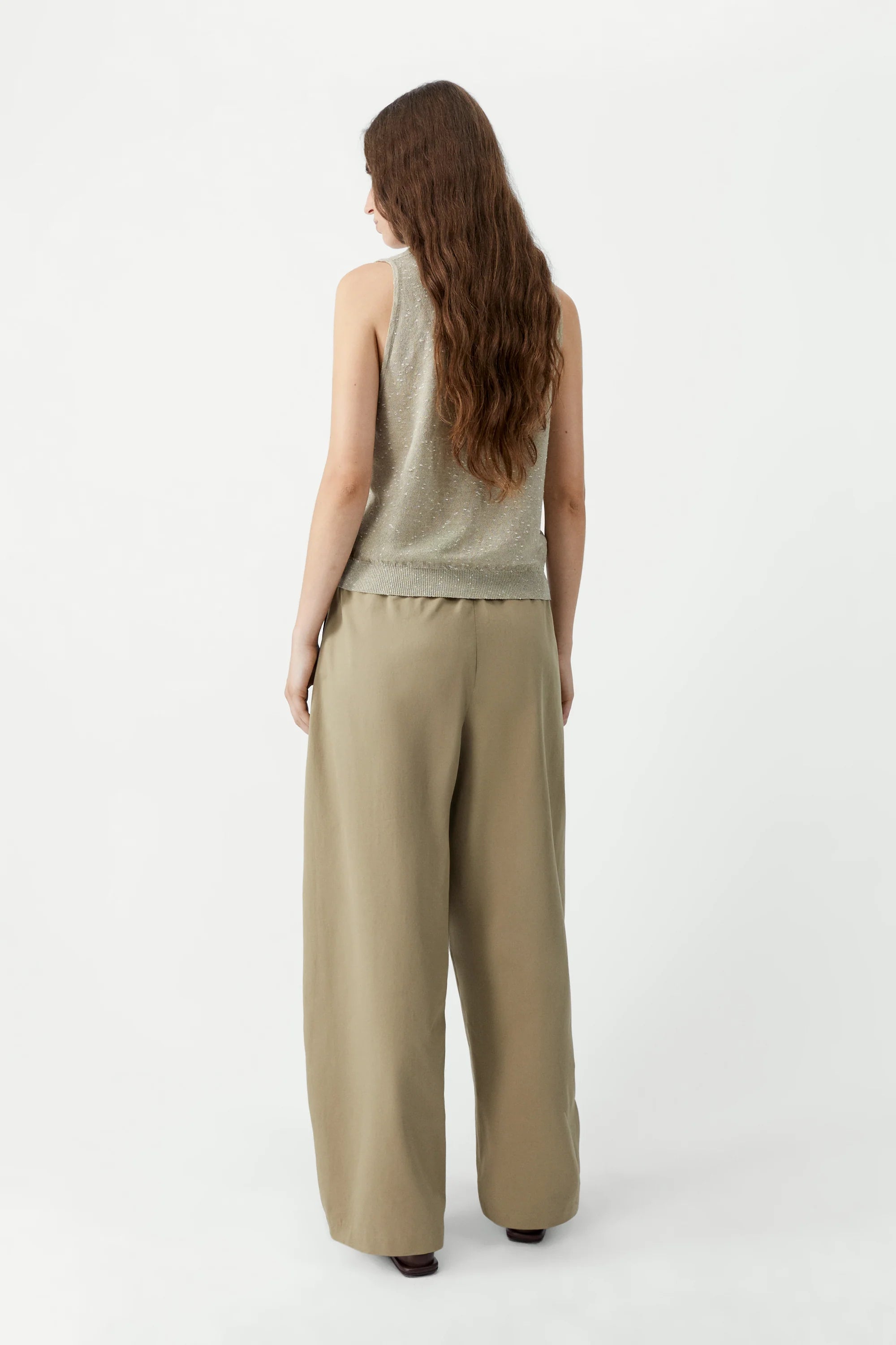 Woman wearing a beige sleeveless top and wide-leg pants on a white background