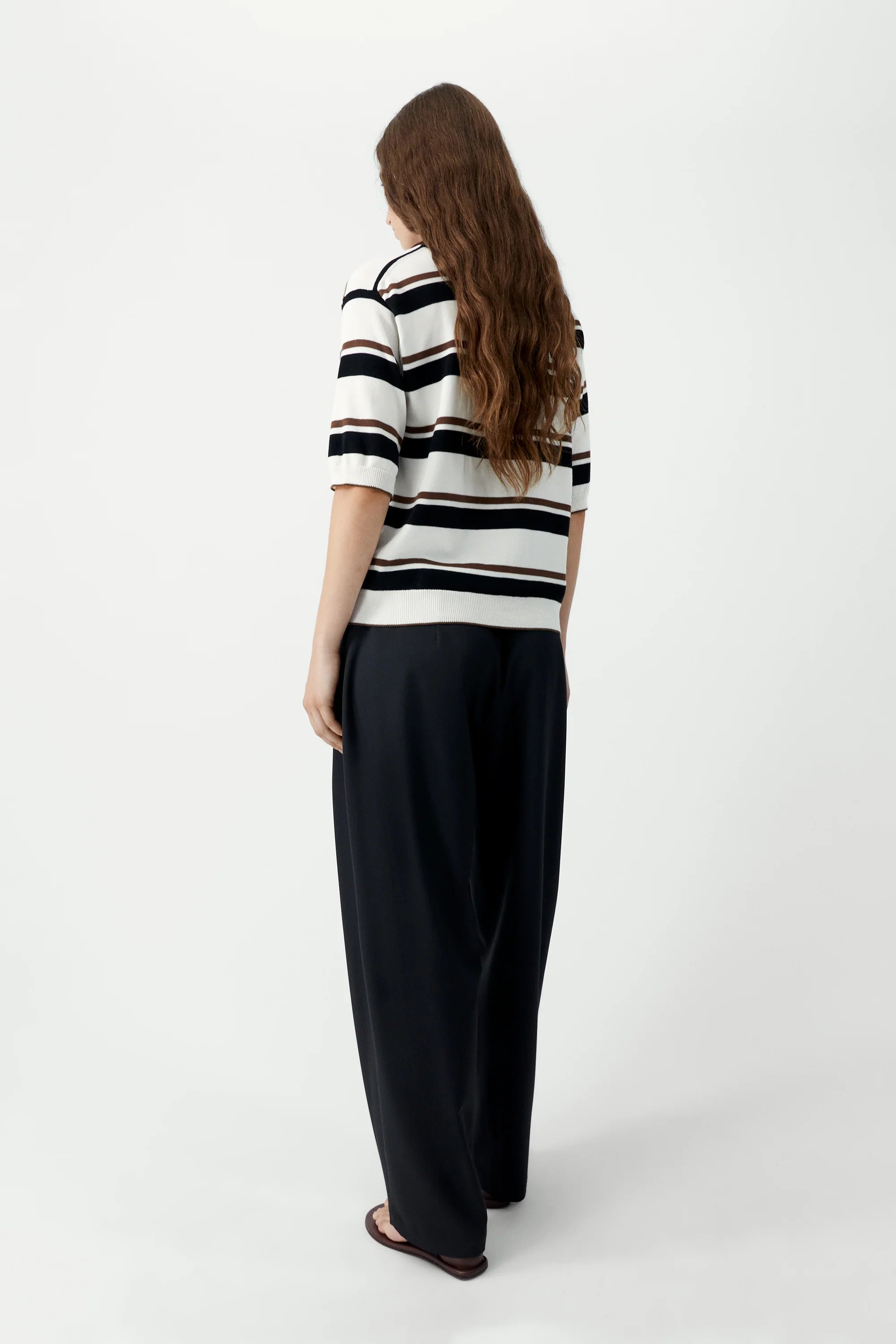 Person wearing a black and white striped shirt and black pants on a white background