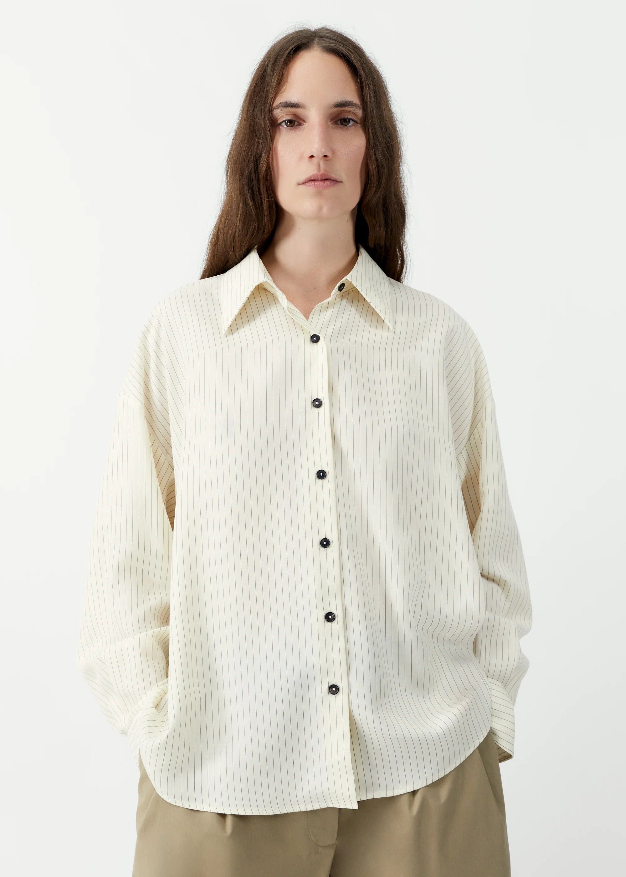 Person wearing a cream ribbed sweater over a collared shirt with beige pants on a white background