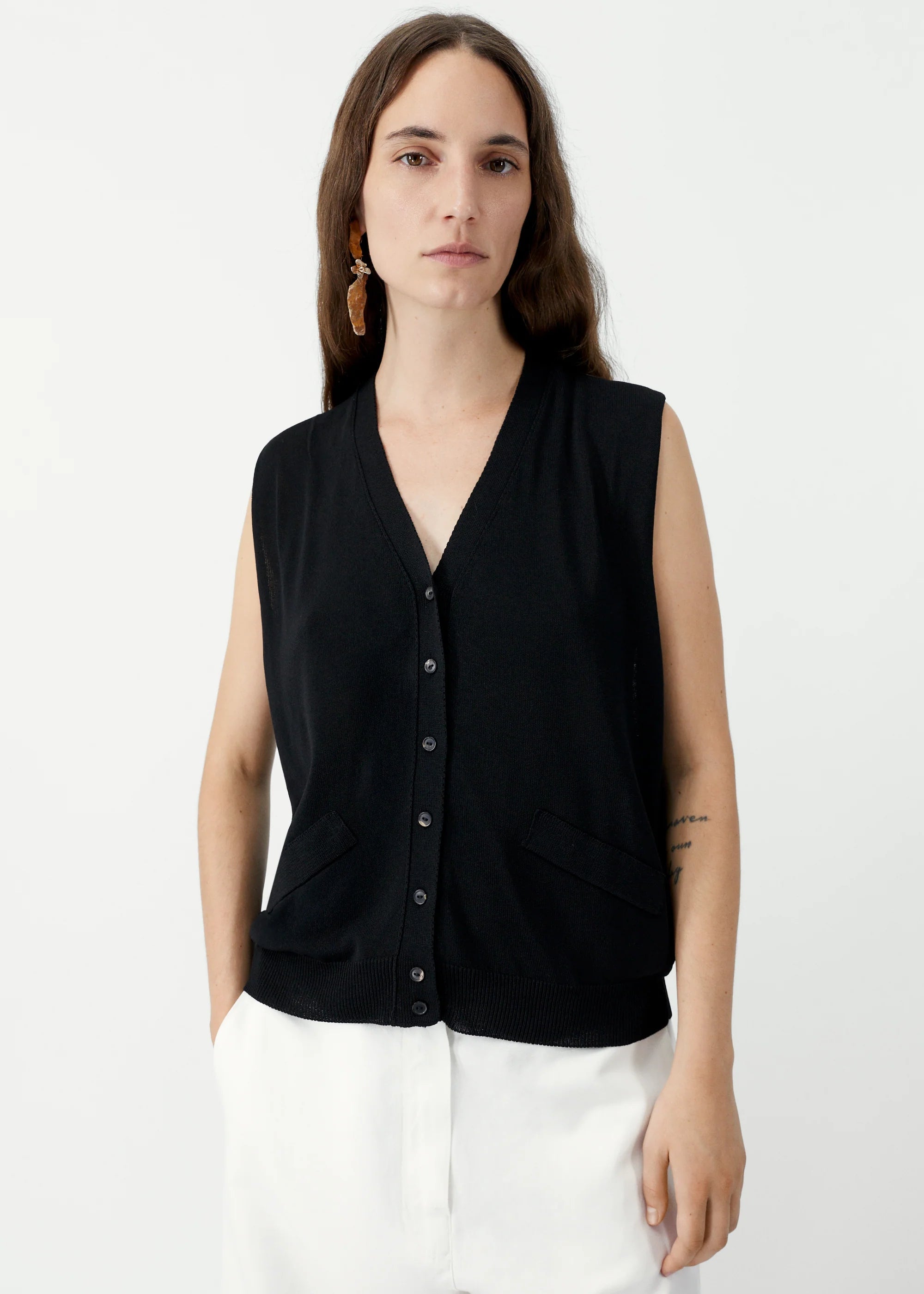 Woman wearing a black sleeveless blouse with buttons on a white background