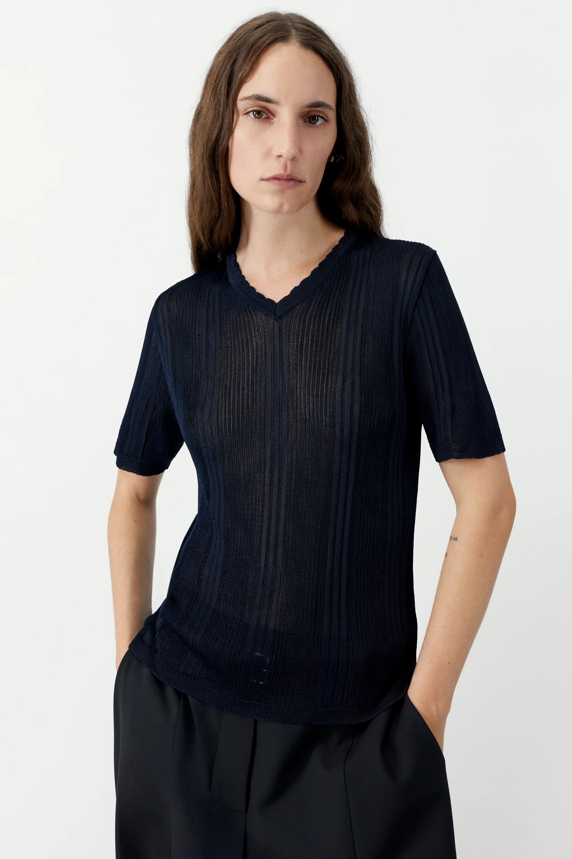 Person wearing a dark blue ribbed t-shirt and black pants on a white background