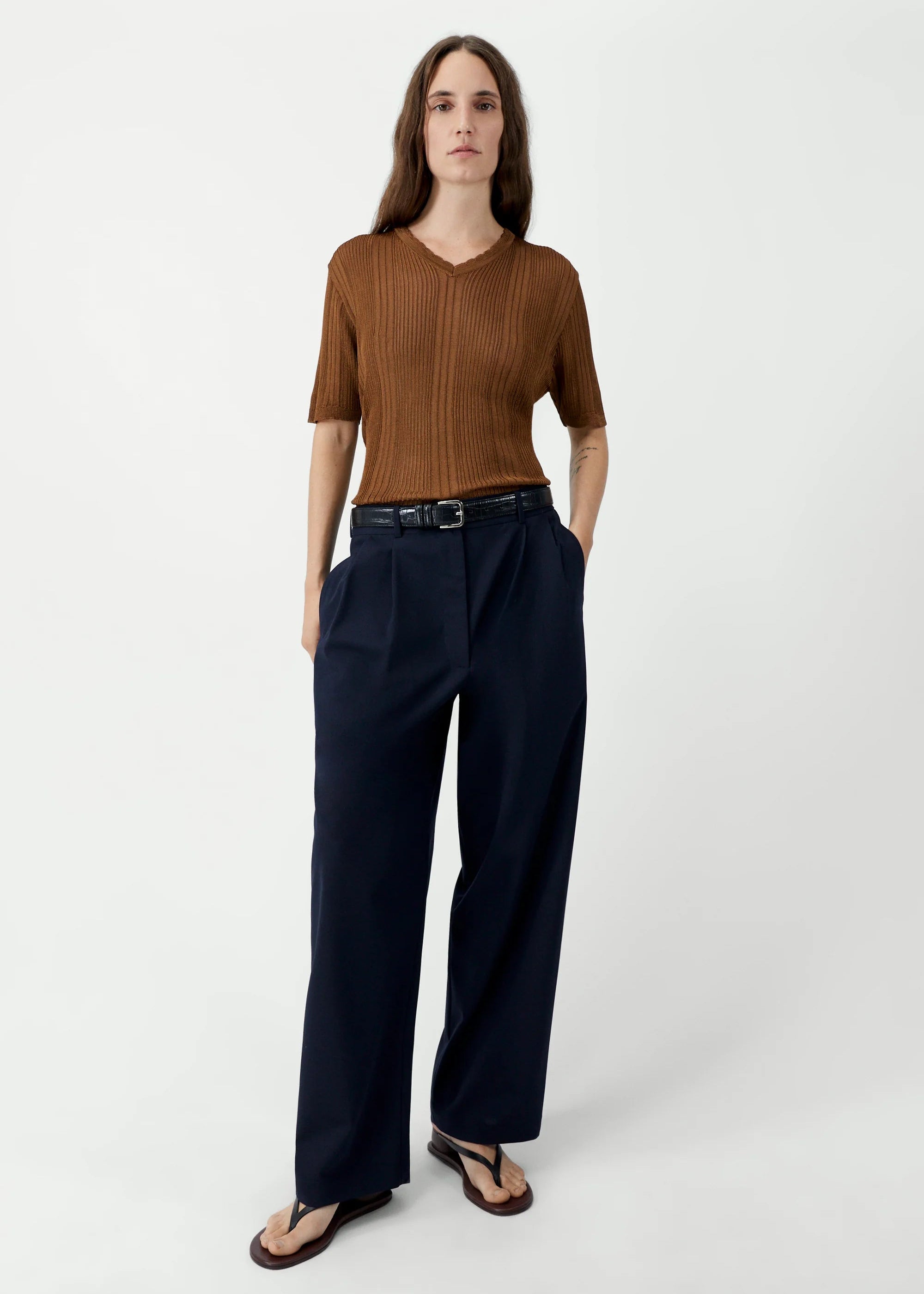 Woman wearing a brown top and navy pants on a white background