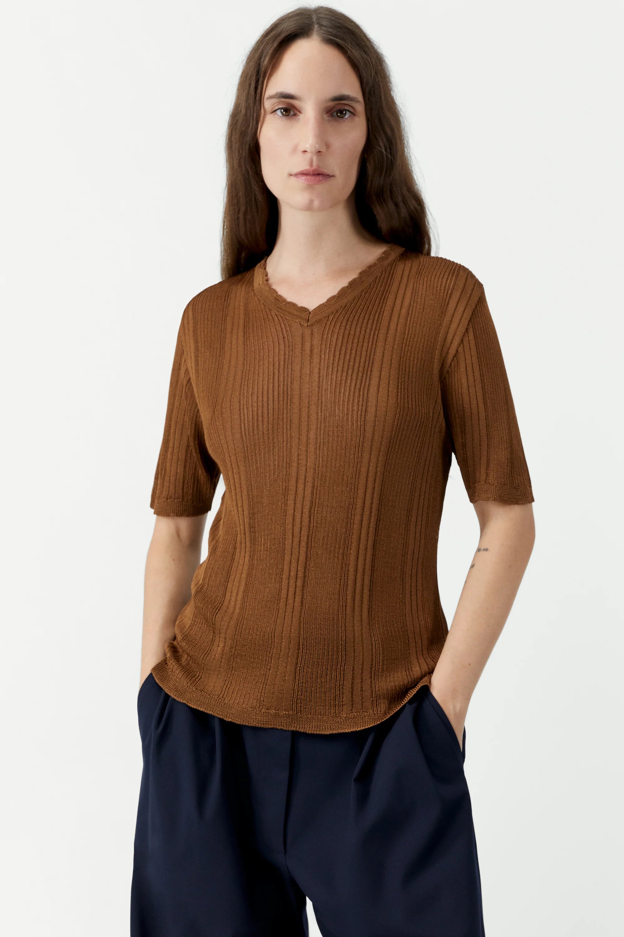 Person wearing a brown ribbed sweater and dark pants on a white background