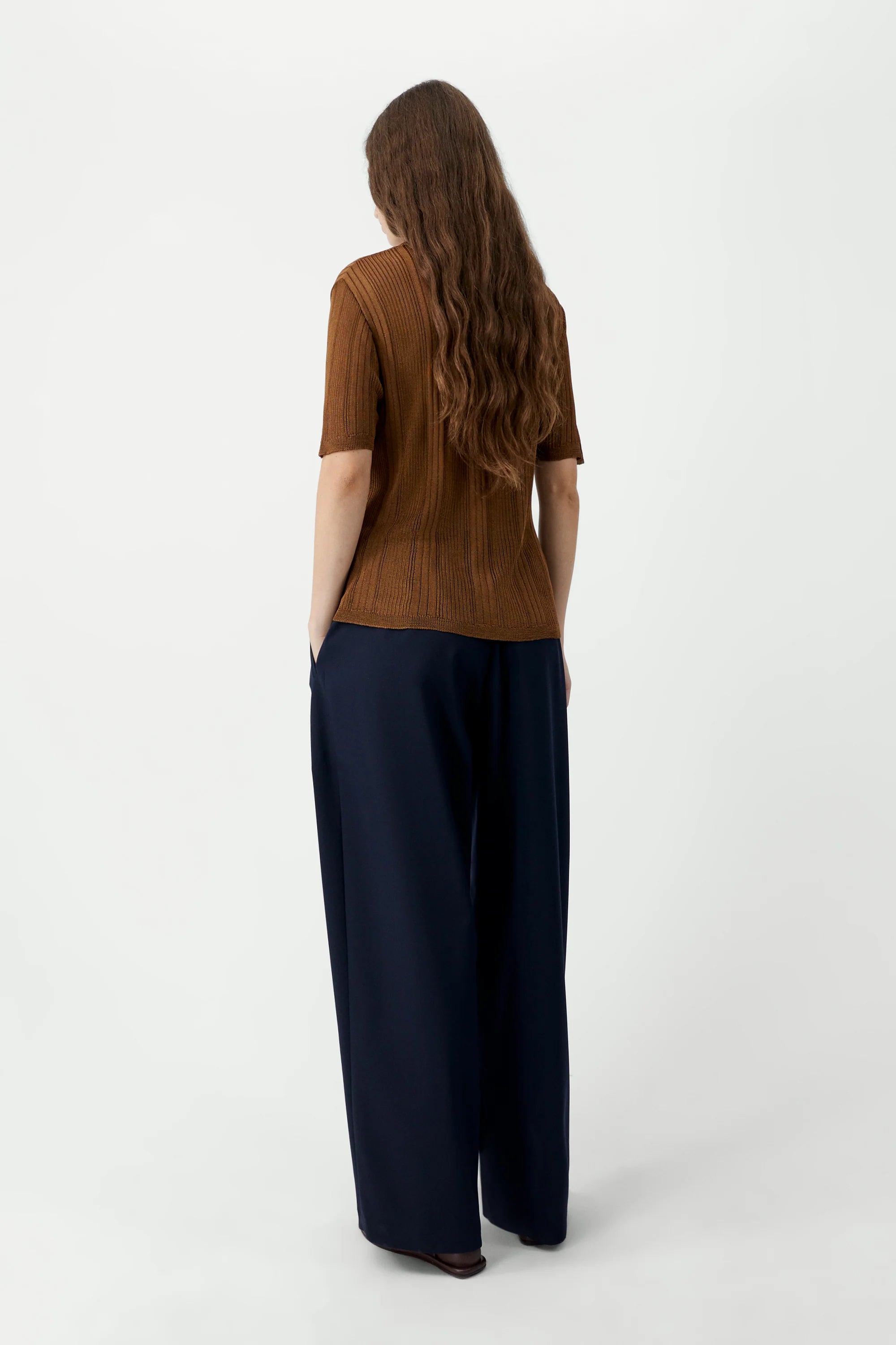Person wearing a brown top and dark blue pants on a white background