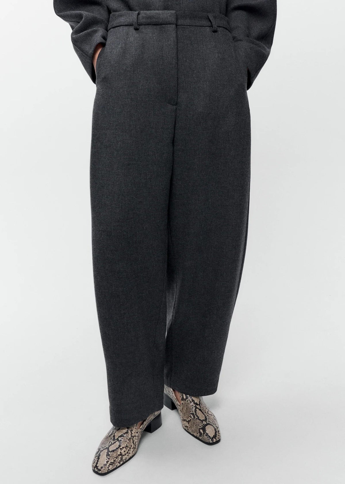 A person wearing dark charcoal gray wide-leg trousers with a matching belt, paired with snakeskin-patterned shoes, shown from the waist down against a light gray studio background.