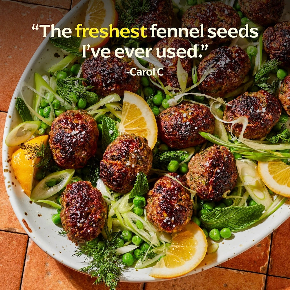 Platter of meatballs with fennel, peas, and lemon slices on a wooden surface.