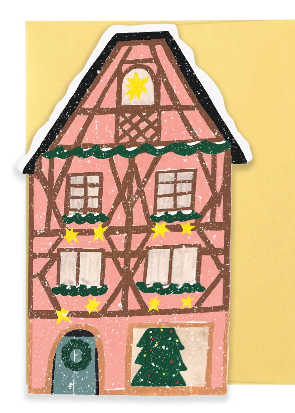 A handcrafted Christmas house card or sticker with a pink facade, brown timber framing, green garlands, a yellow star, and a small tree at the bottom, shown against a pale yellow background.