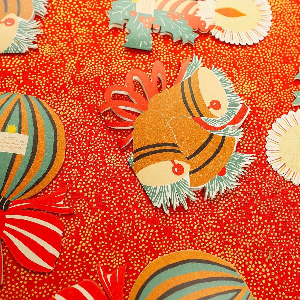 A close-up of a colorful Christmas-themed paper craft or card design featuring striped ornaments, holly, and a central ornament on a red dotted background.