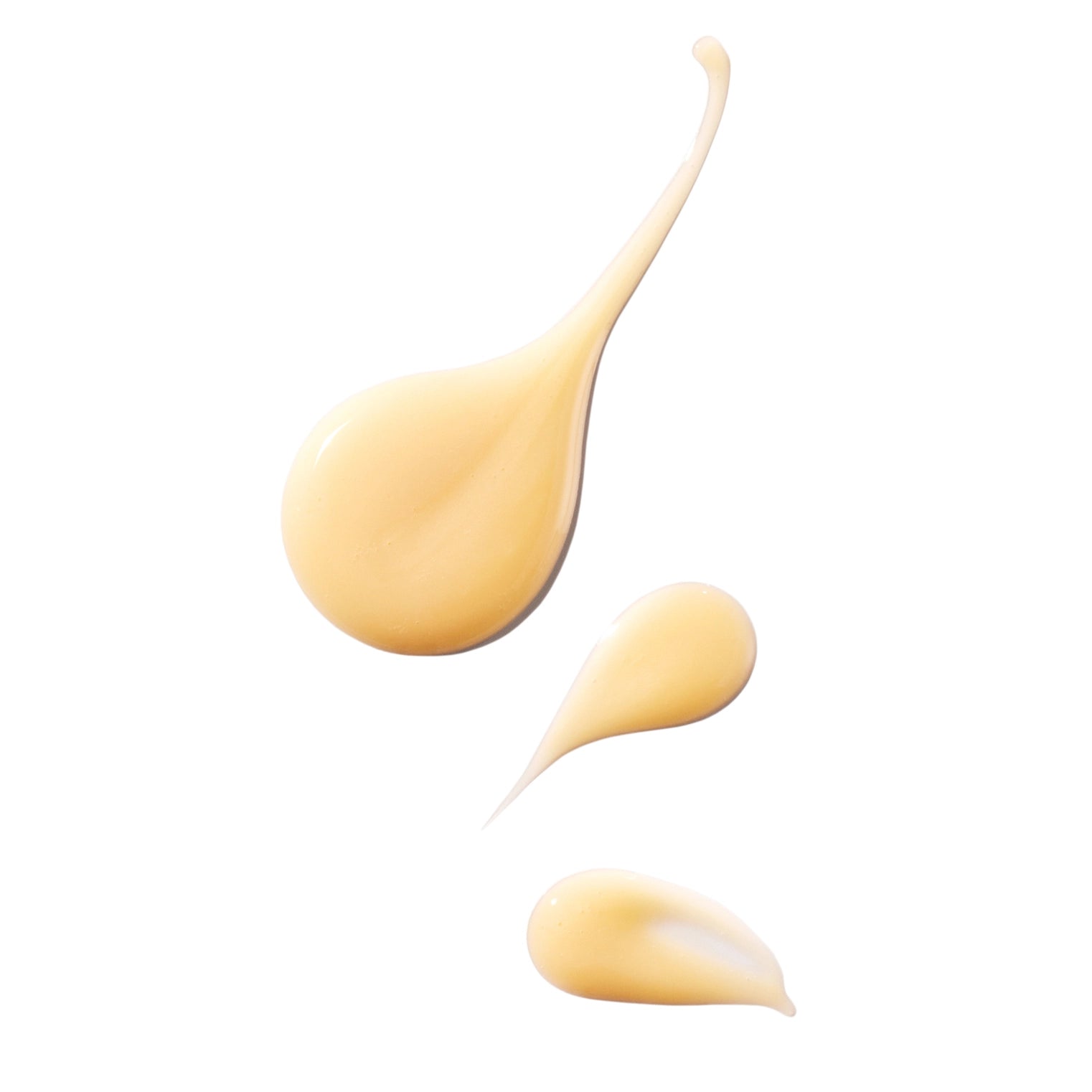 Three droplets of yellow cream on a white background