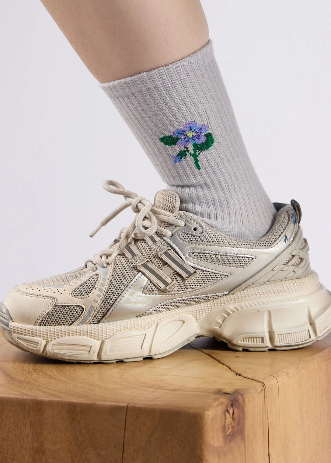 Beige sneakers worn with a sock featuring a floral design on a light background