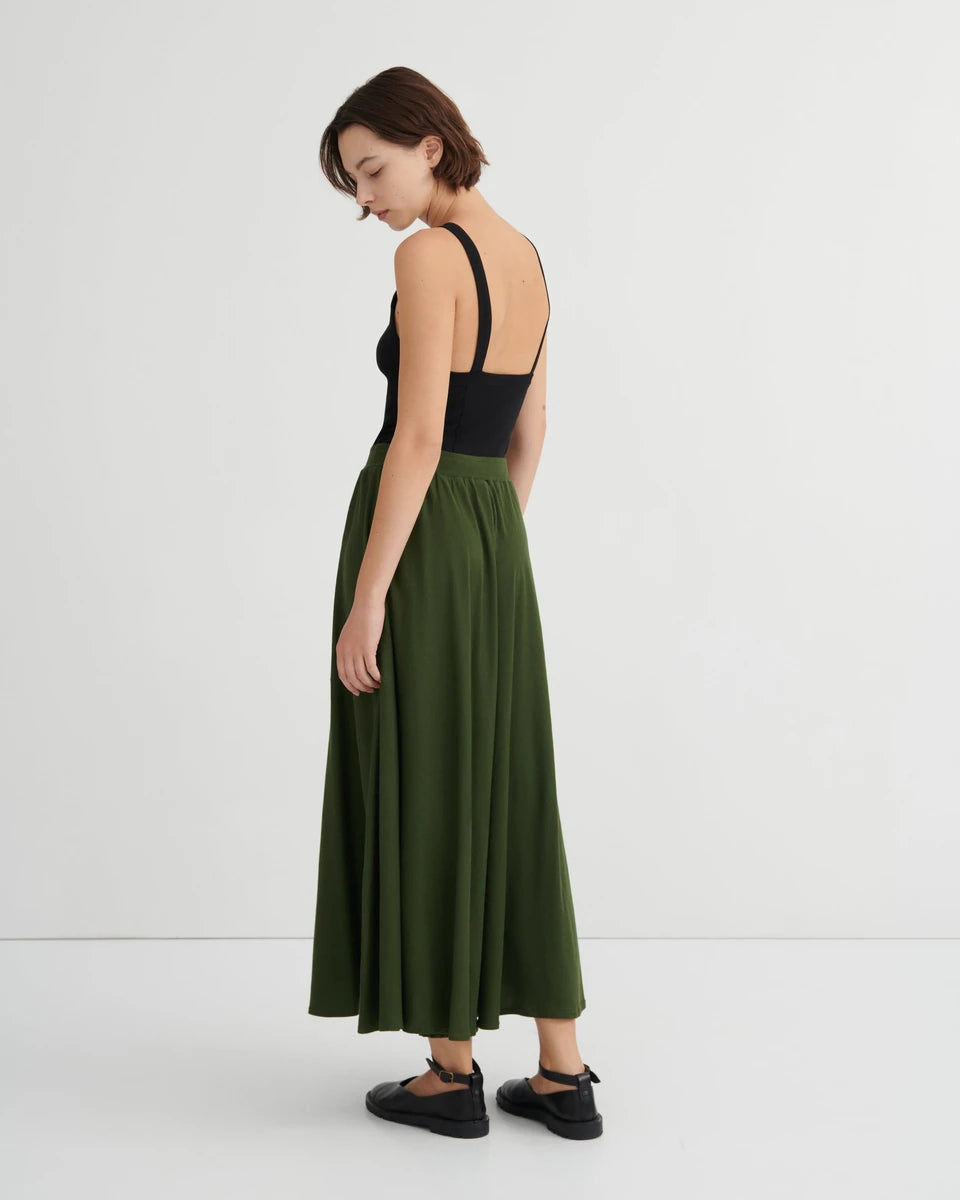 model wearing long green skirt with black tank and black shoes from back