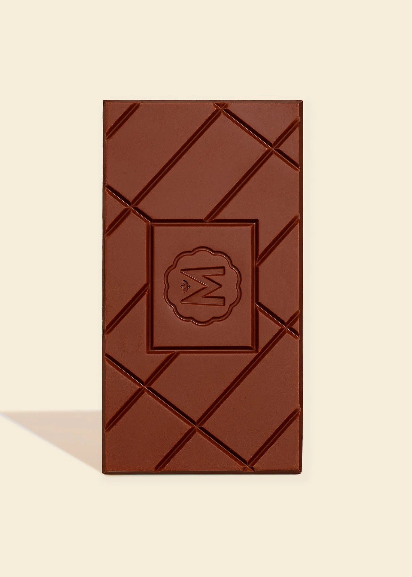 A single dark chocolate bar with a diagonal crisscross pattern and a central embossed logo, set against a solid cream background with a soft shadow.