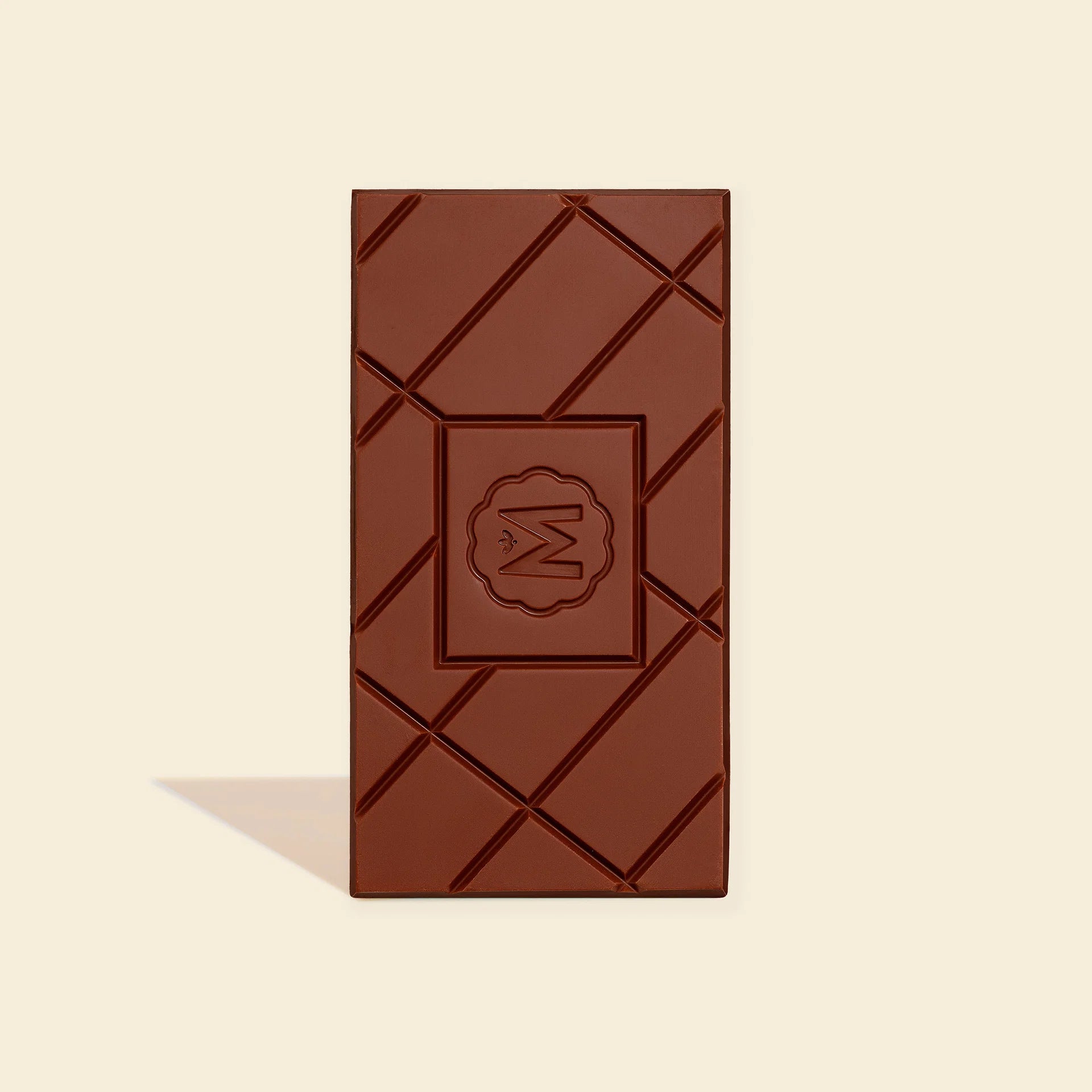 A single dark chocolate bar with a diagonal crisscross pattern and a central embossed logo, set against a solid cream background with a soft shadow.